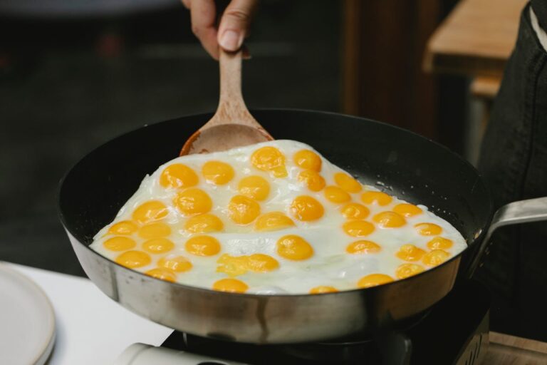 Cooking quail eggs in a pan with a wooden spatula, showcasing fresh breakfast preparation.